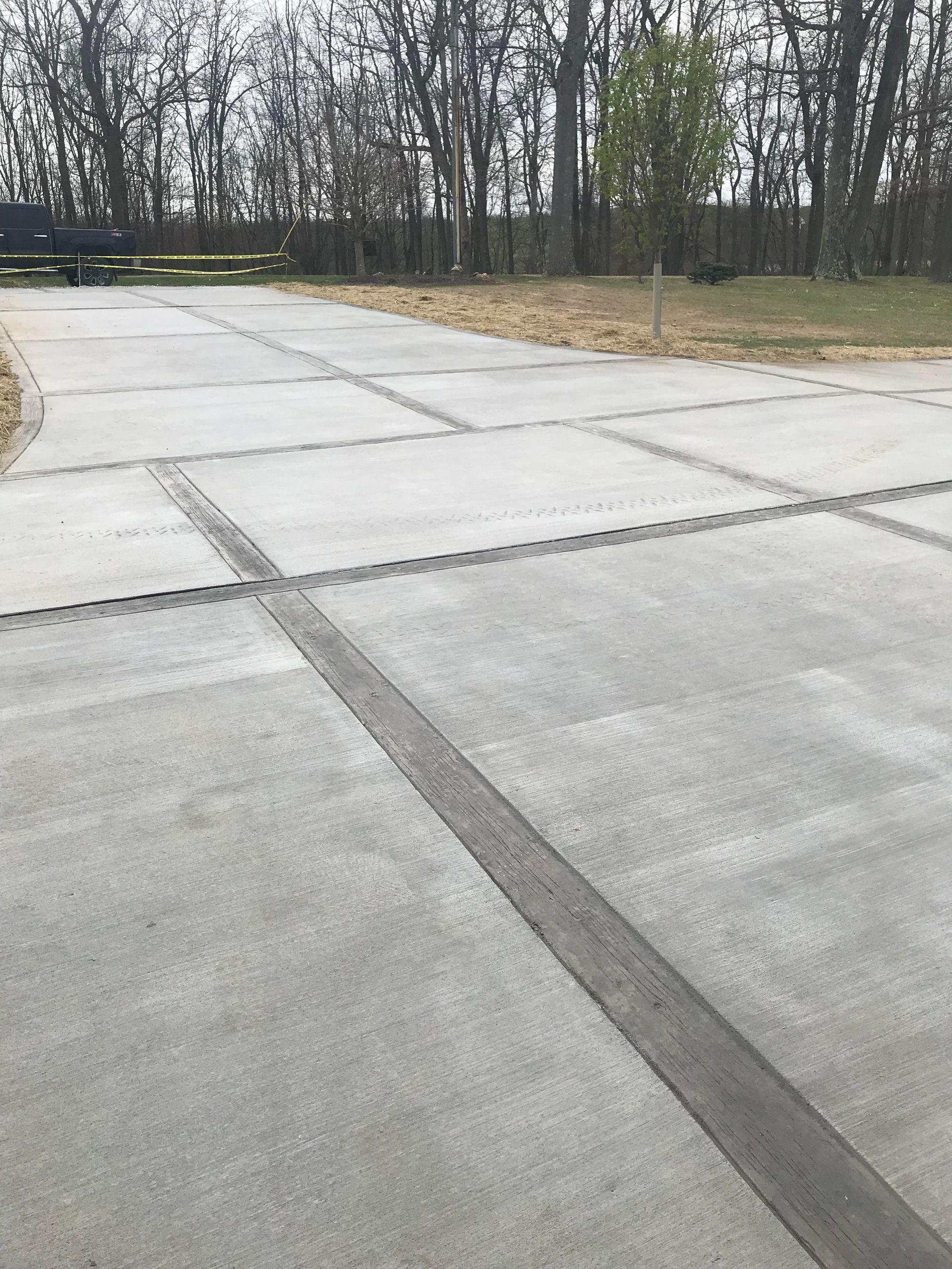 Empty concrete driveway with control joints, bordered by bare trees and grass.