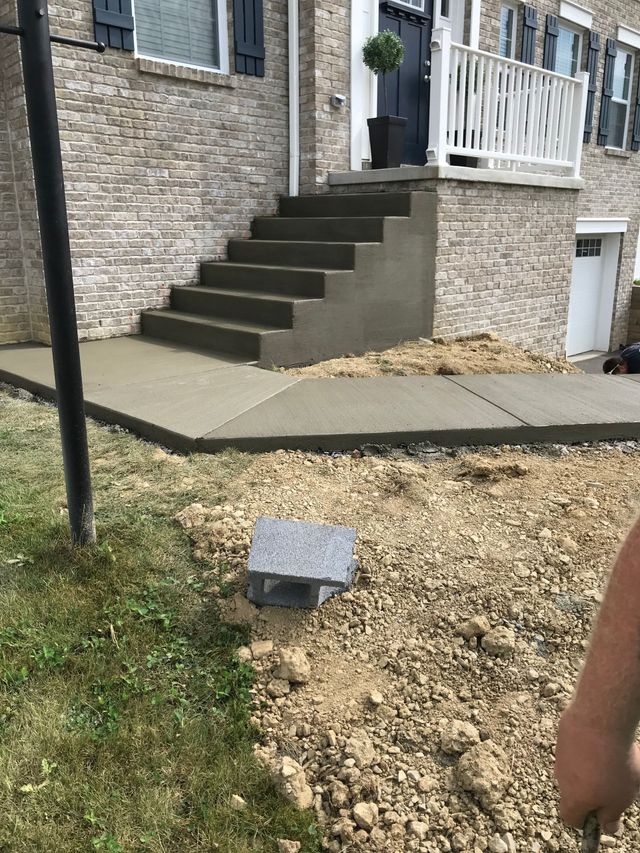 Concrete front steps beside a brick house, with a gravel yard and a small utility box in the foreground.