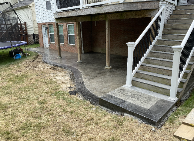 Backyard patio with brick house, concrete slab, and white exterior stairs leading to an upper deck