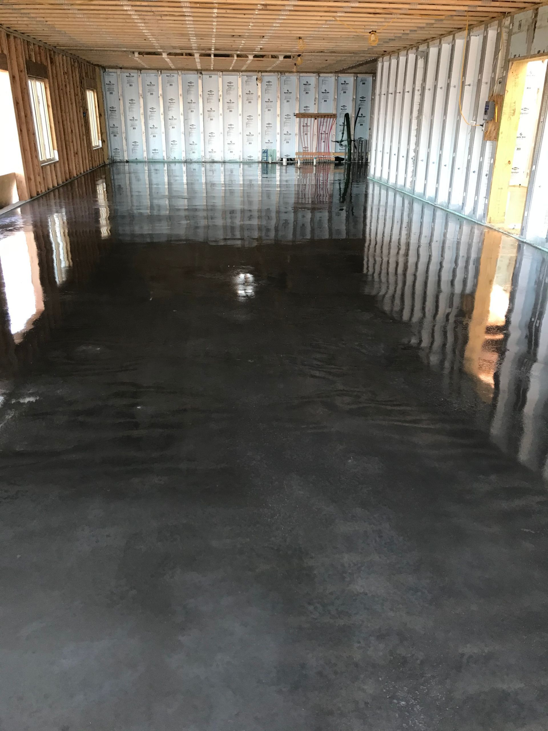 Empty unfinished room with a glossy black floor, exposed wooden ceiling, and insulated walls.