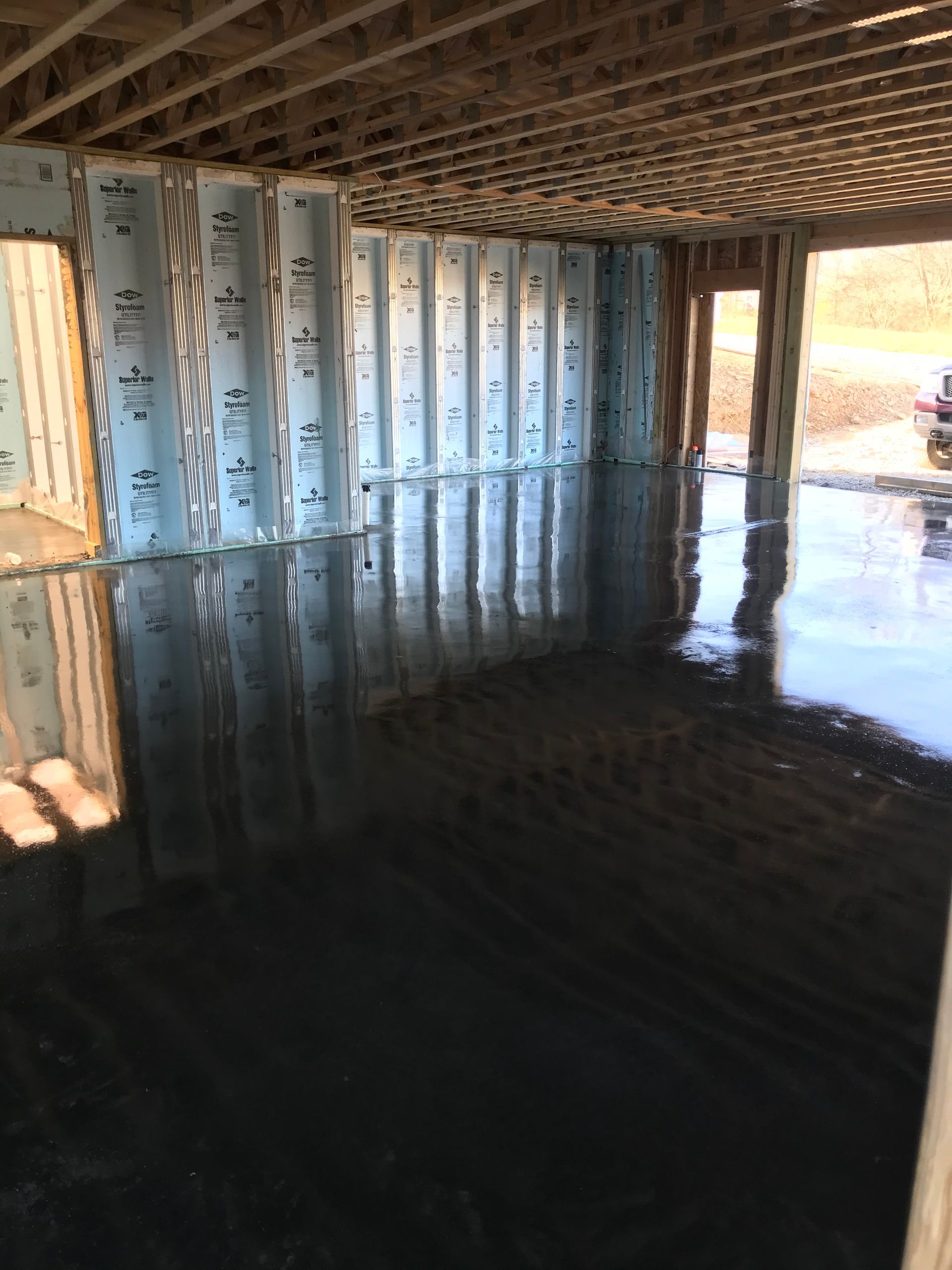 Interior of a flooded room with reflective dark water, exposed wall framing, and open doorway to daylight