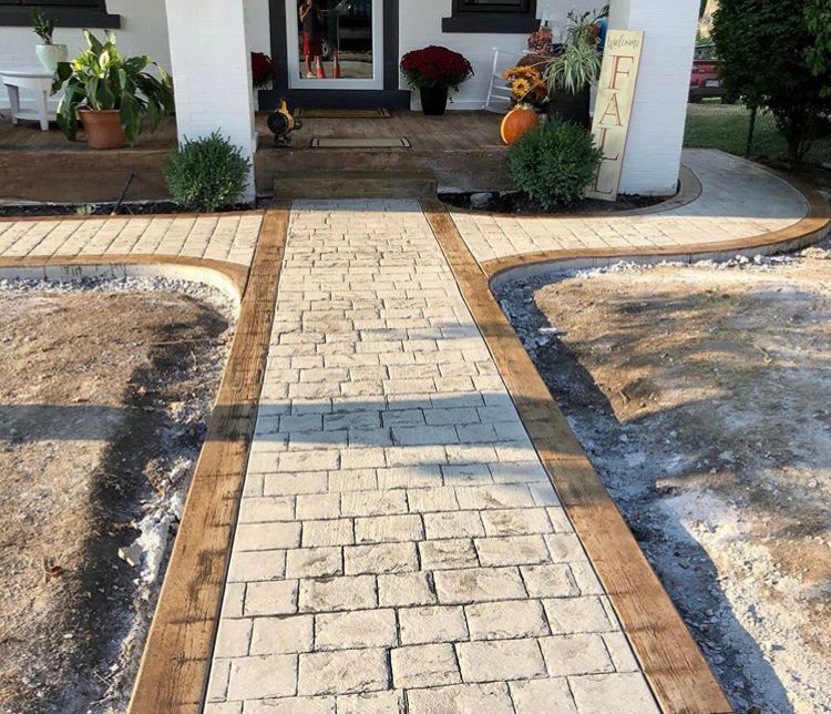Brick walkway leading to a front porch, bordered by black edging and bare landscaping beds.