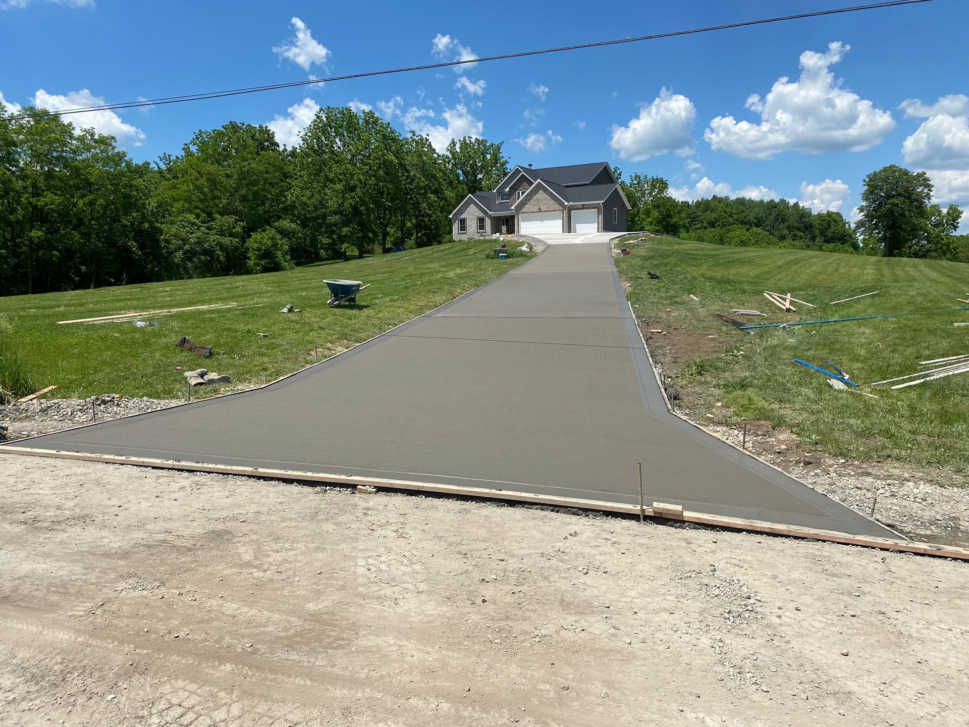 Freshly poured driveway leading to a white house on a grassy lot under a blue sky