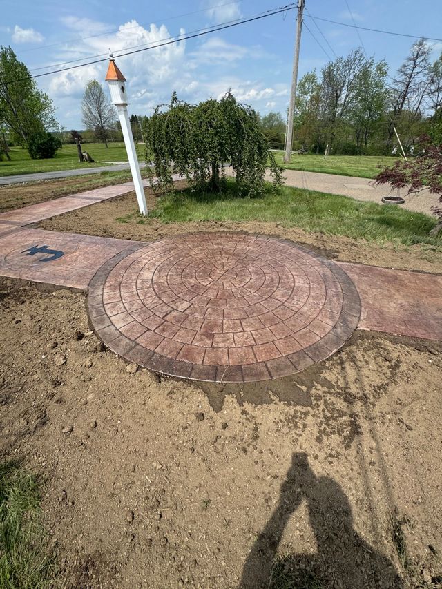 Outdoor brick patio with circular stone pad, grassy yard, and a white lamp post under a sunny sky