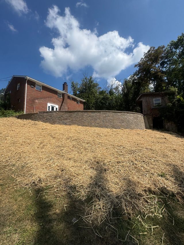 Brick house beside a stone wall on a grassy hill under a blue sky with clouds