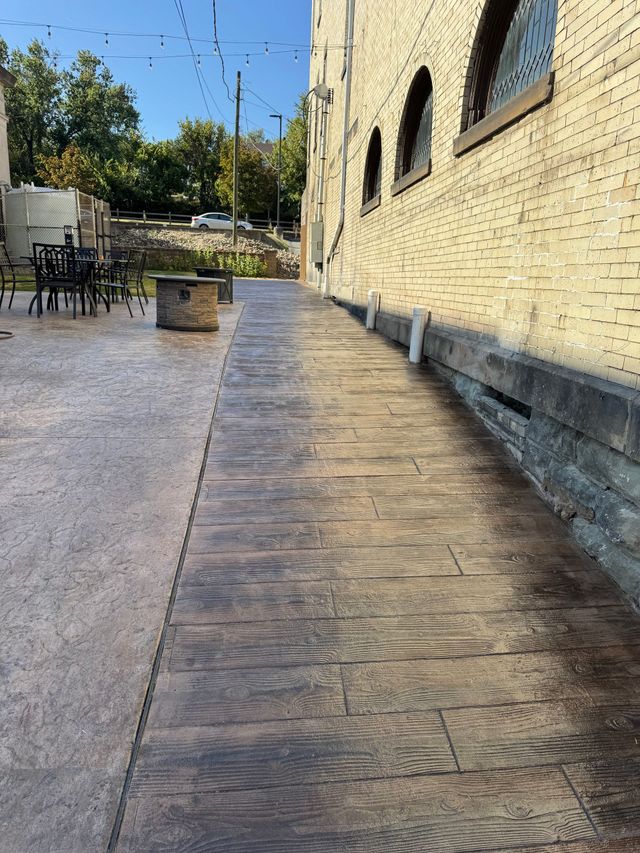 Sunlit stone walkway beside a yellow brick building with arched windows and a small planter.