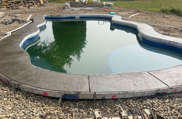 Partially filled backyard pool with green water and a white concrete edge, surrounded by gravel