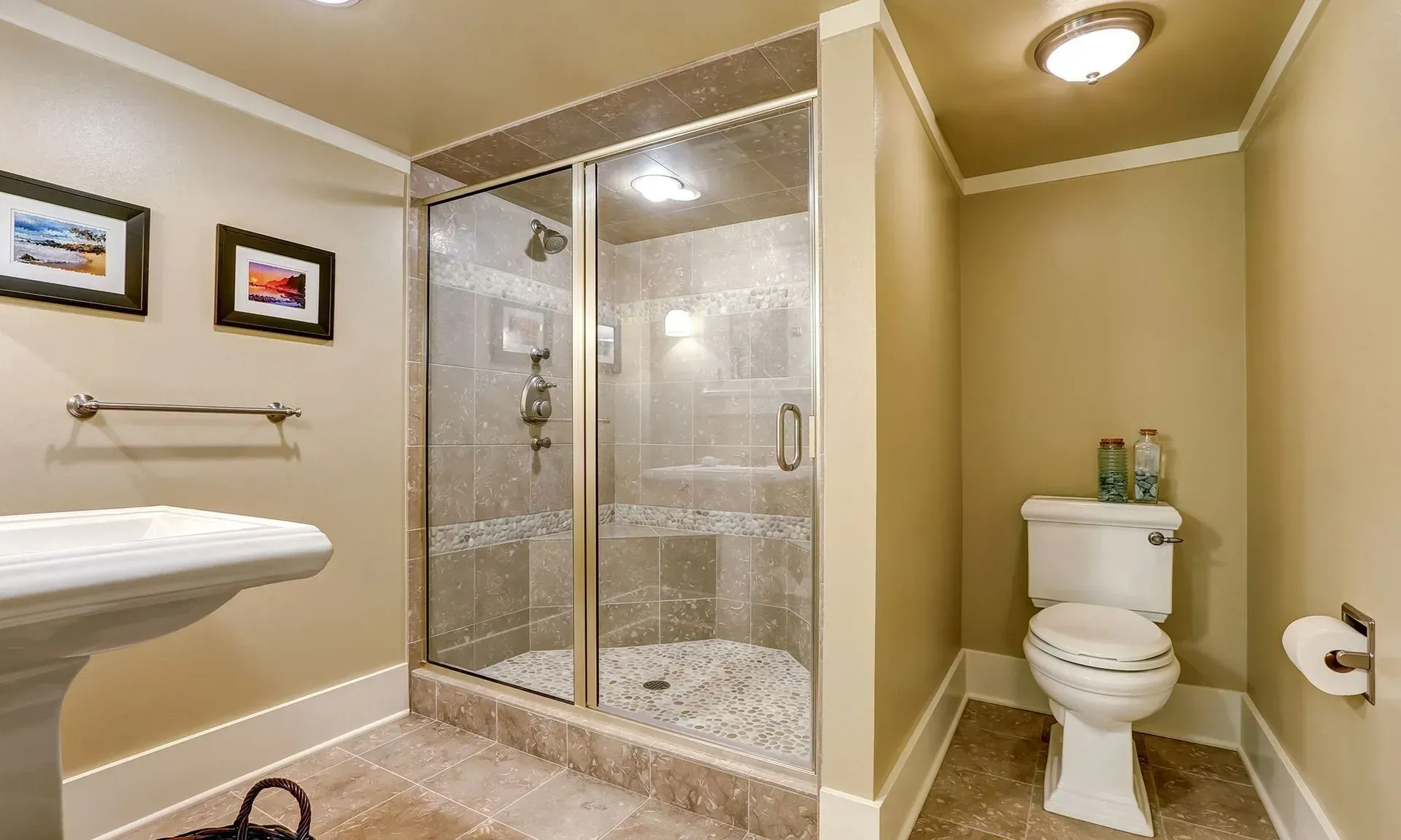 Small beige bathroom with glass shower, wall art, sink, and toilet under a ceiling light.
