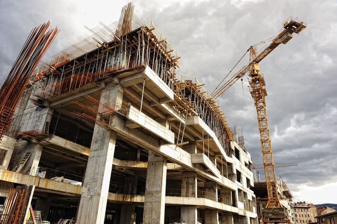 Partially built concrete building with cranes at a construction site under cloudy sky