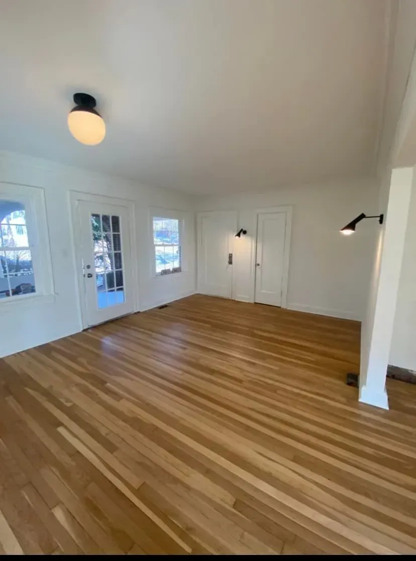 Empty room with hardwood floors, white walls, French doors, and a ceiling light.