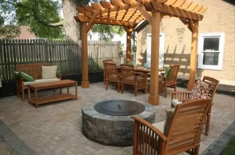 Patio with wooden pergola, fire pit, bench, and chairs around a paved courtyard