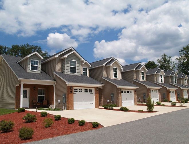 Row of modern suburban houses with garages, red mulch landscaping, and a partly cloudy sky