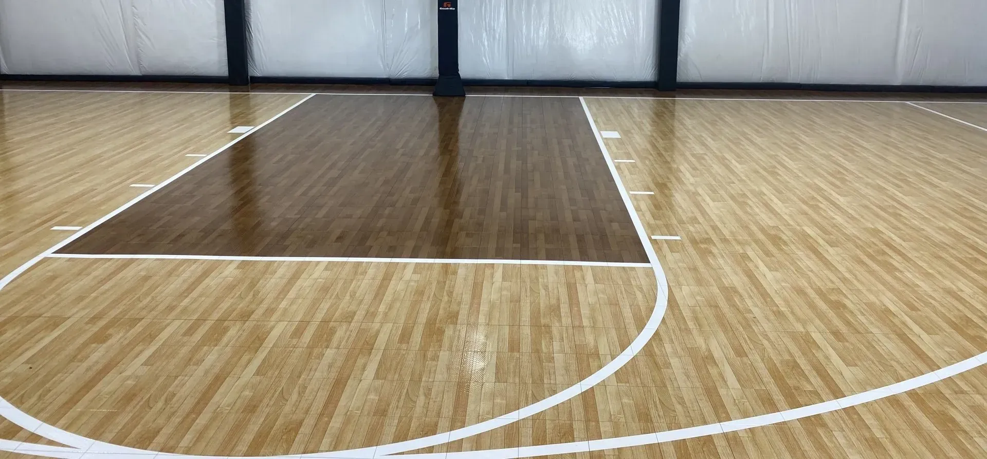 Wooden basketball court with brown and light wood sections, white lines.