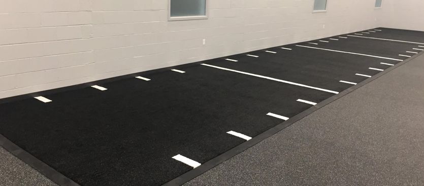 Black exercise mat with white lines against a gray wall.