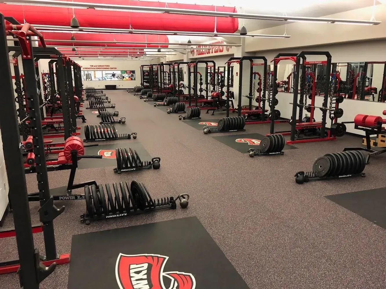 Weight room with multiple weight racks, weights, and kettlebells. Red and black color scheme.