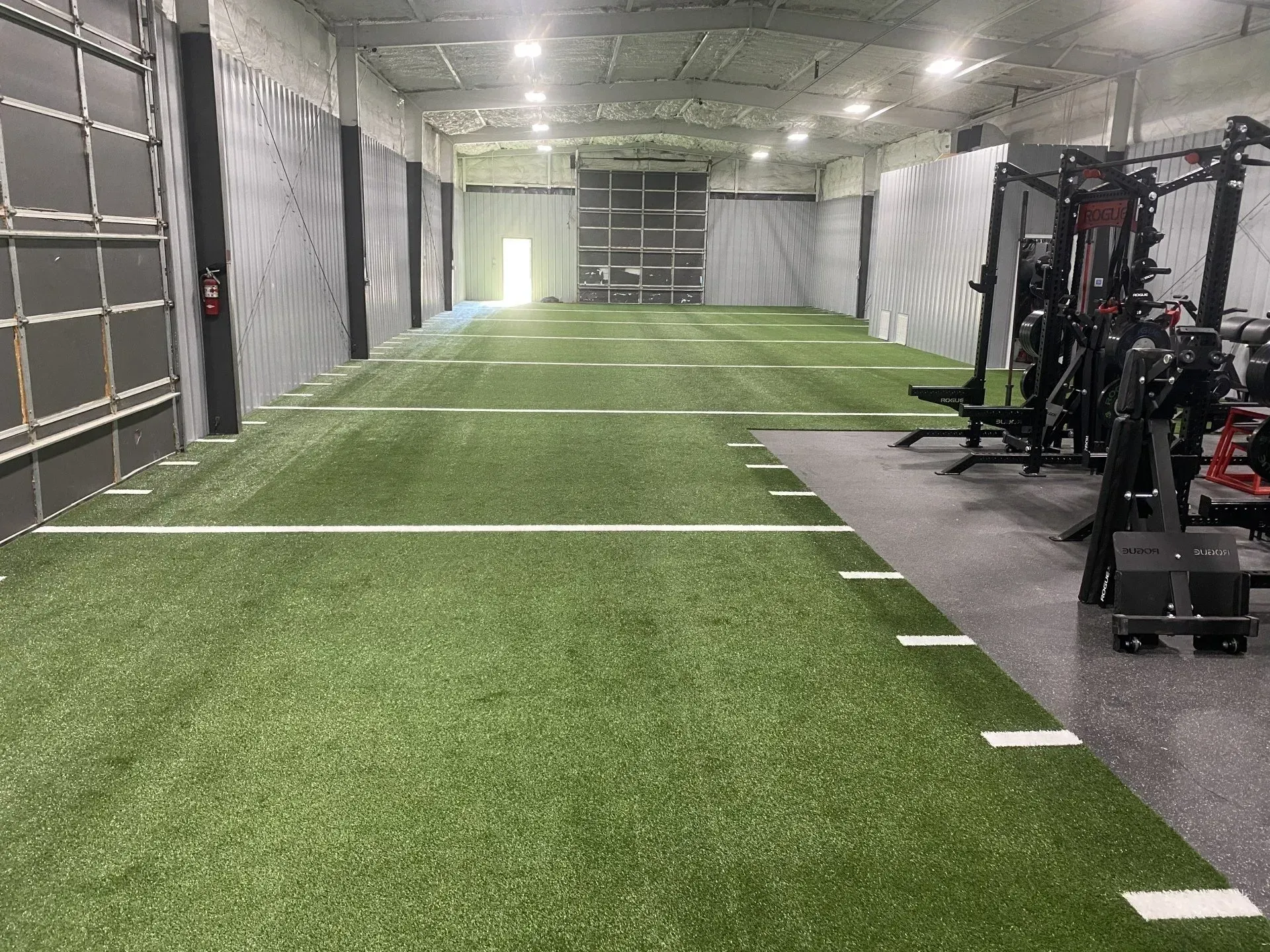 Indoor training facility with green turf, white yard lines, and weight equipment.