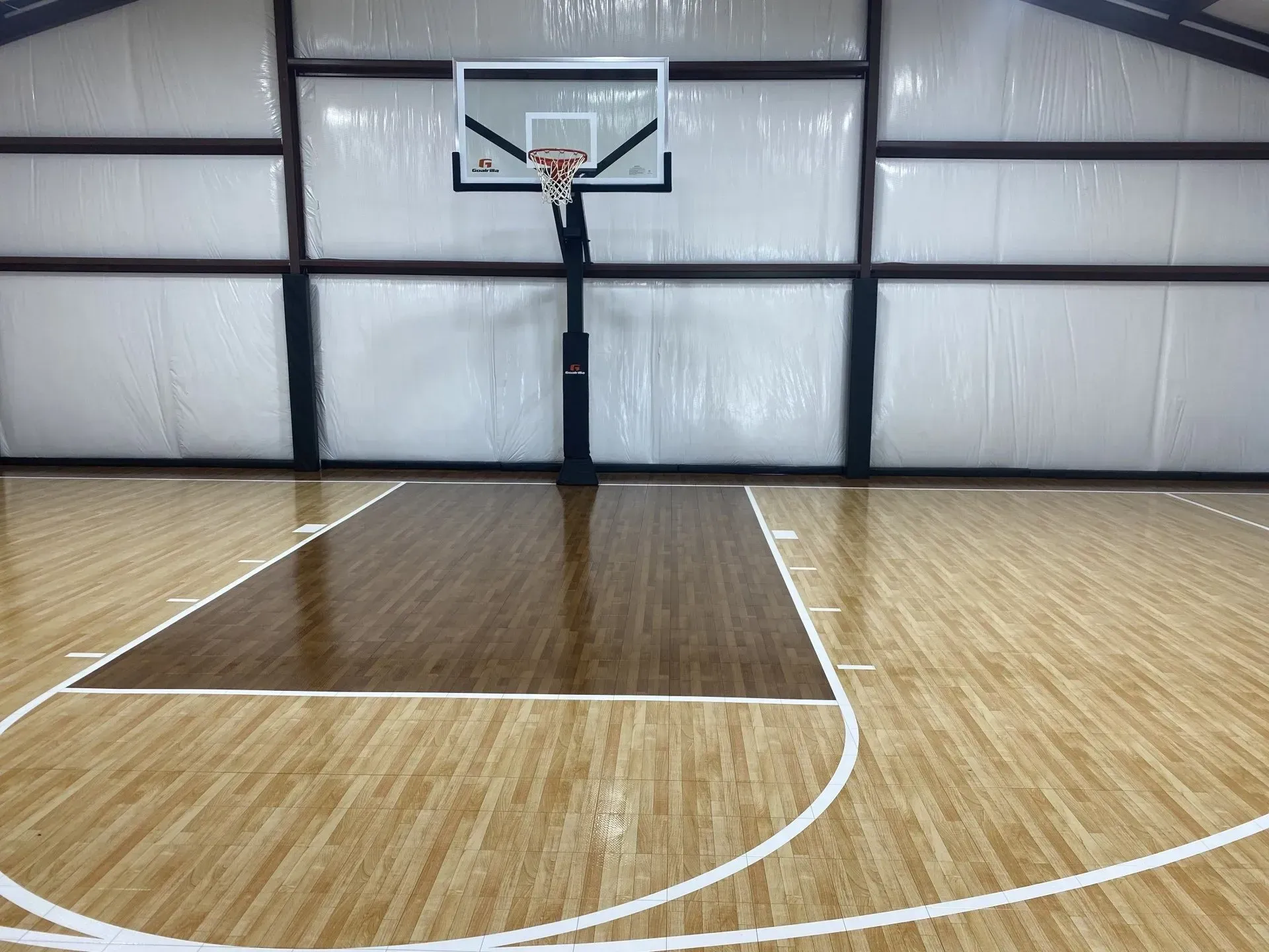 Basketball court with hardwood floor, hoop, and backboard; brown key area, white court lines, inside a building.