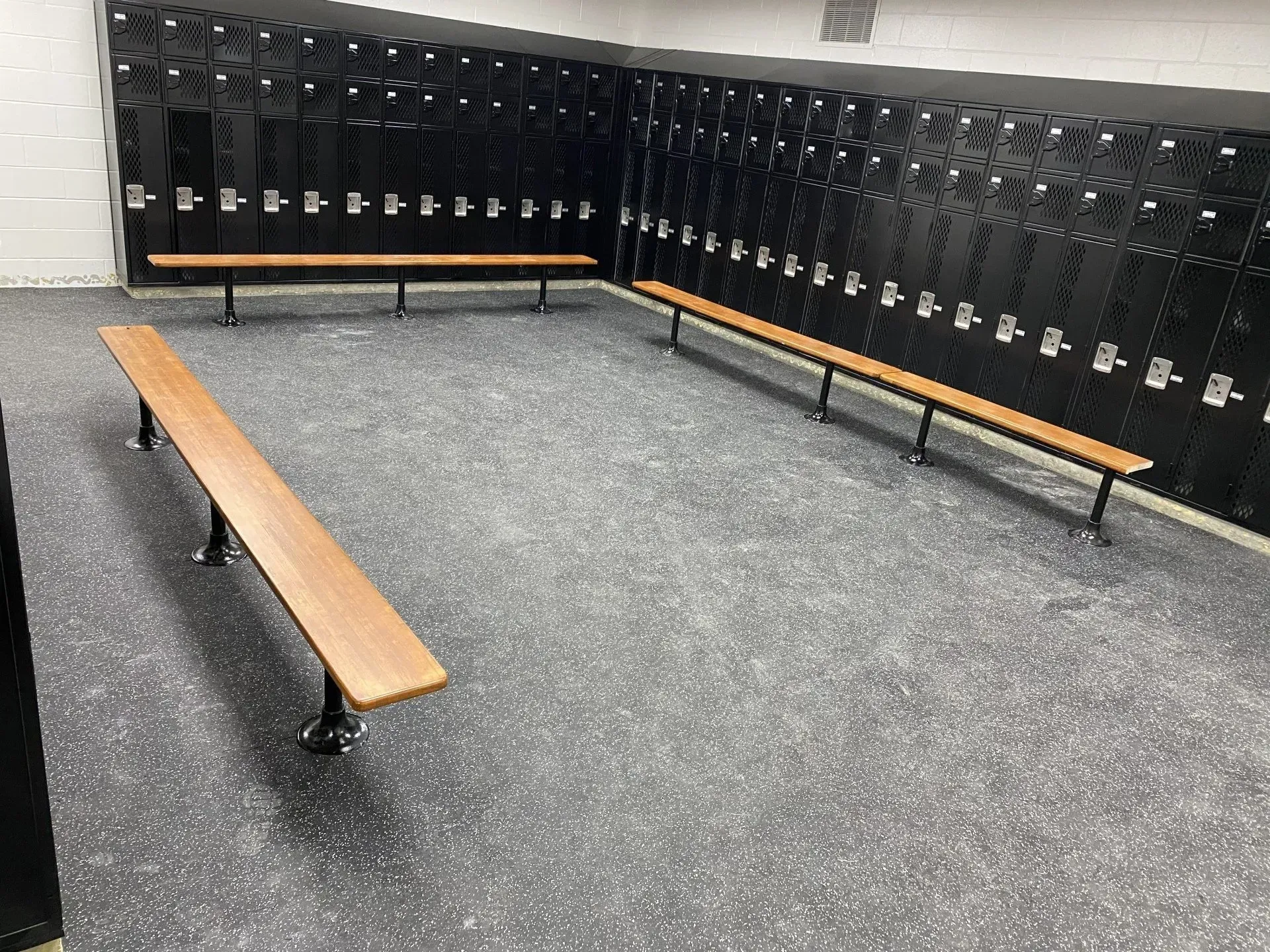 A locker room with black lockers, wooden benches, and a speckled gray floor.