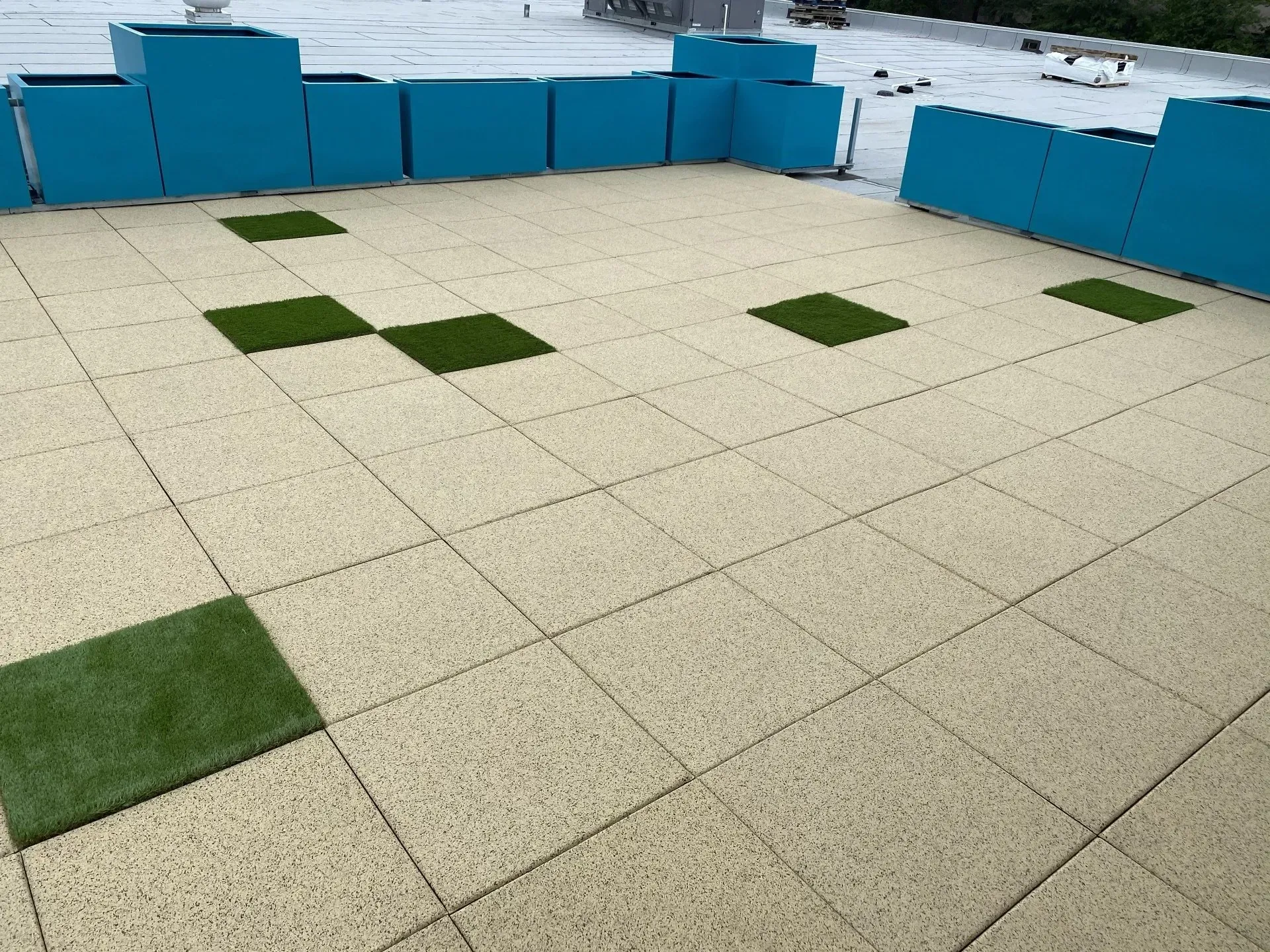 Outdoor patio with beige tiles, teal planters, and green artificial grass squares.