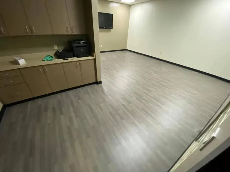Empty office space with gray wood-look flooring, light walls, and brown cabinetry.