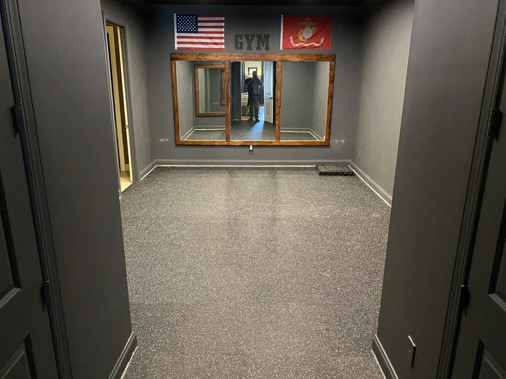 Gym interior with rubber flooring, grey walls, a triple mirror, and flags.