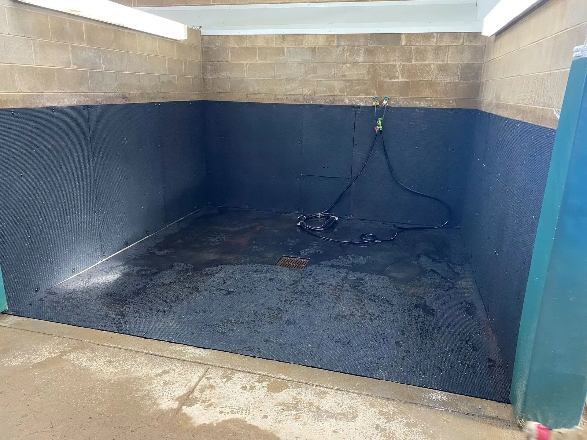 A small, black-walled wash bay with a hose, dirty floor, and concrete block walls.
