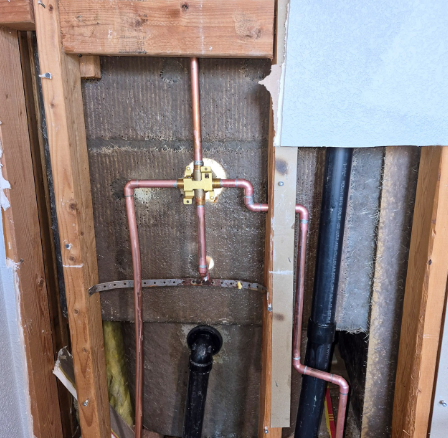 Exposed copper plumbing and a yellow valve inside an unfinished wall cavity.