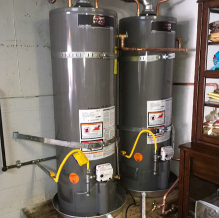 Two tall gray water heaters with yellow gas lines in a utility room