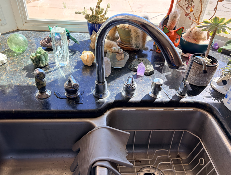 Kitchen sink under a window with crystal decorations and potted plants on the sill