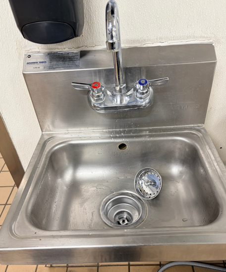 Stainless steel utility sink with running faucet, red and blue handles, and a small dish inside.
