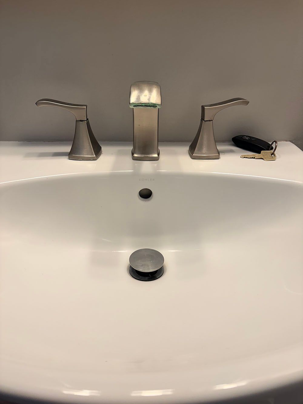 Bathroom sink with chrome faucet, drain stopper, and a small black item on the counter.