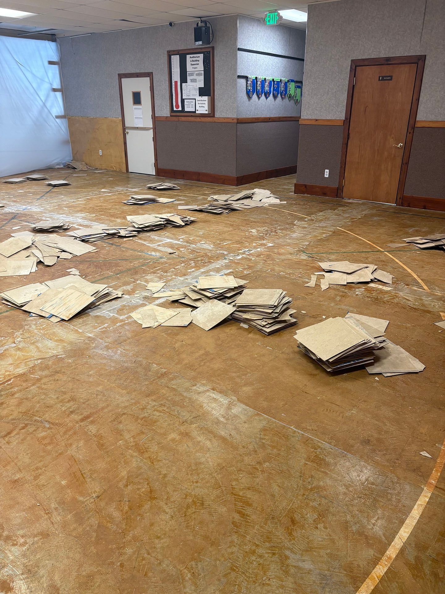 Room with damaged flooring, cardboard pieces scattered on the floor, and doors in the background.
