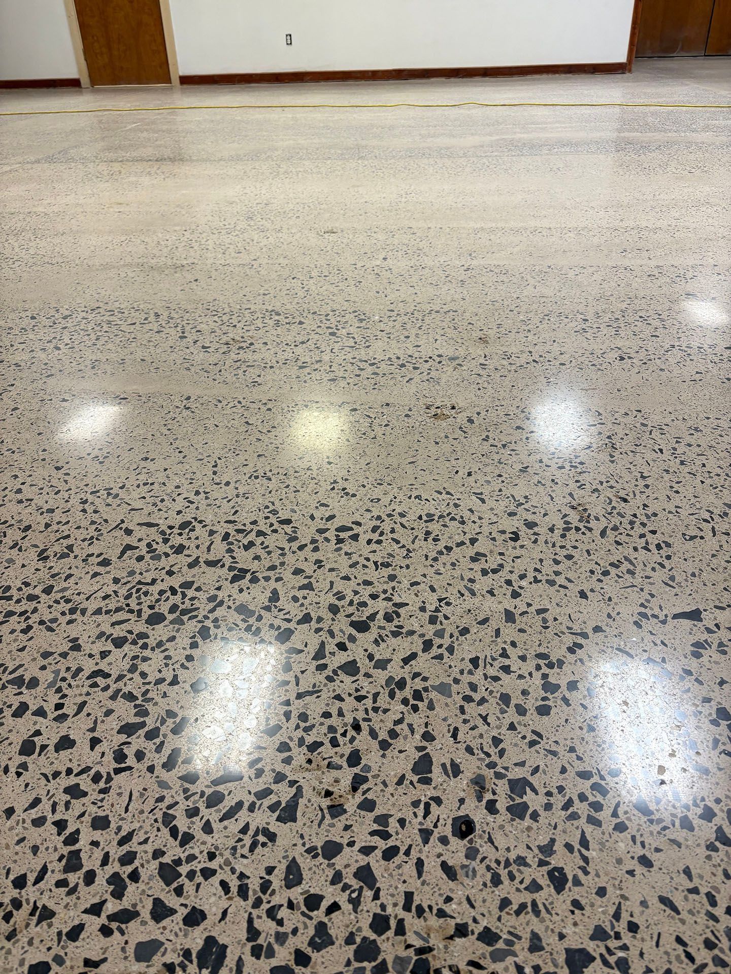 Polished concrete floor in a room, with visible aggregate and reflections of lights.