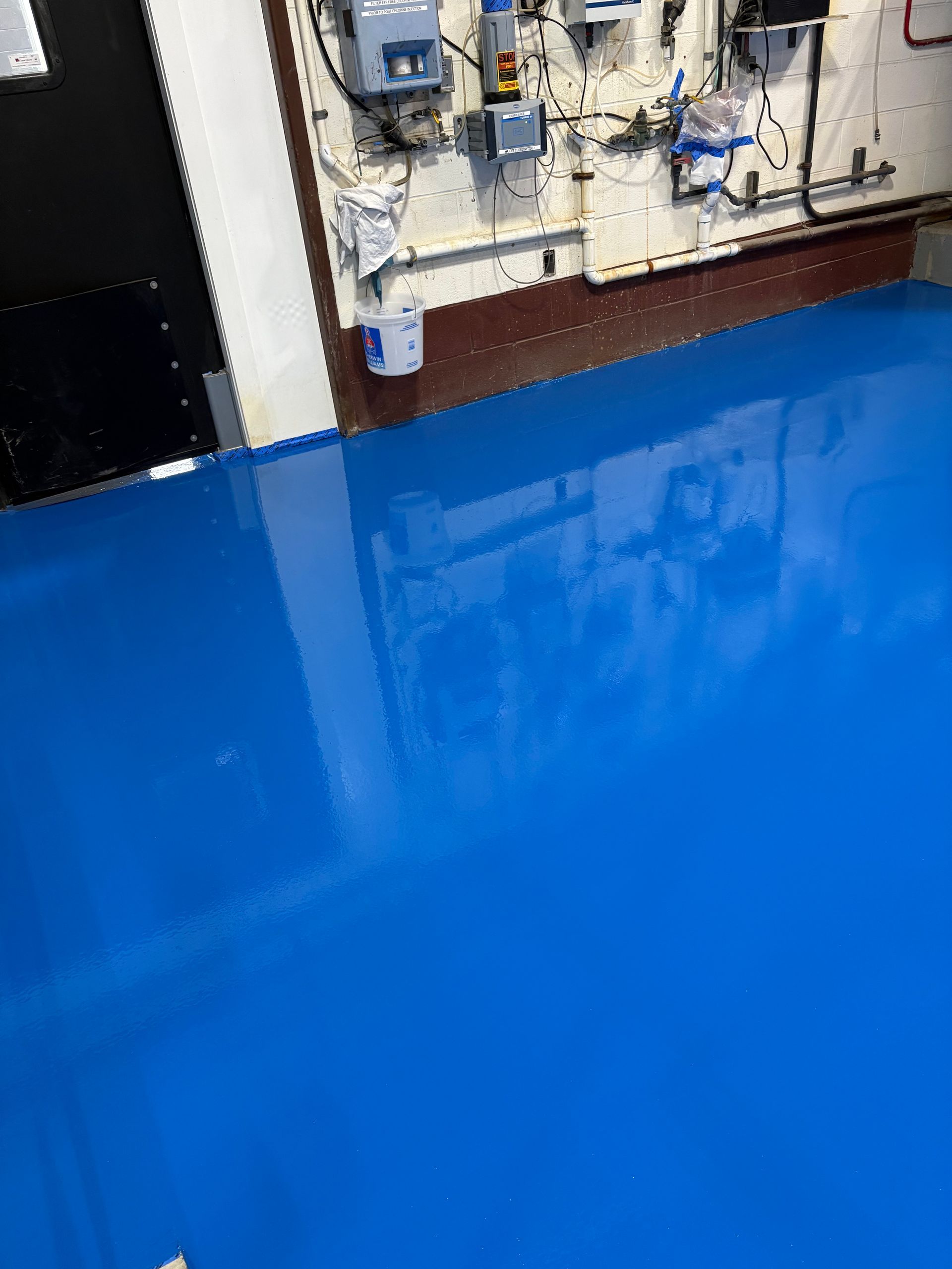 Blue glossy floor with a wall-mounted electrical panel and equipment above it.
