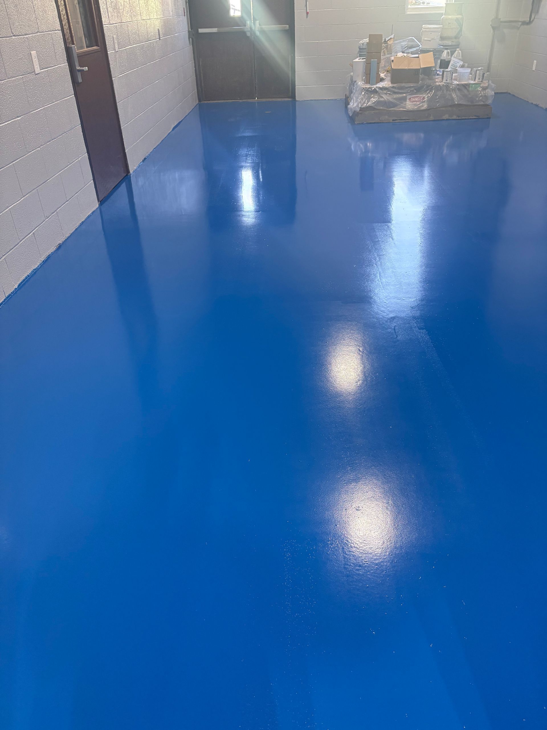 Blue glossy floor in a hallway with brick walls and stacked items near the far end.