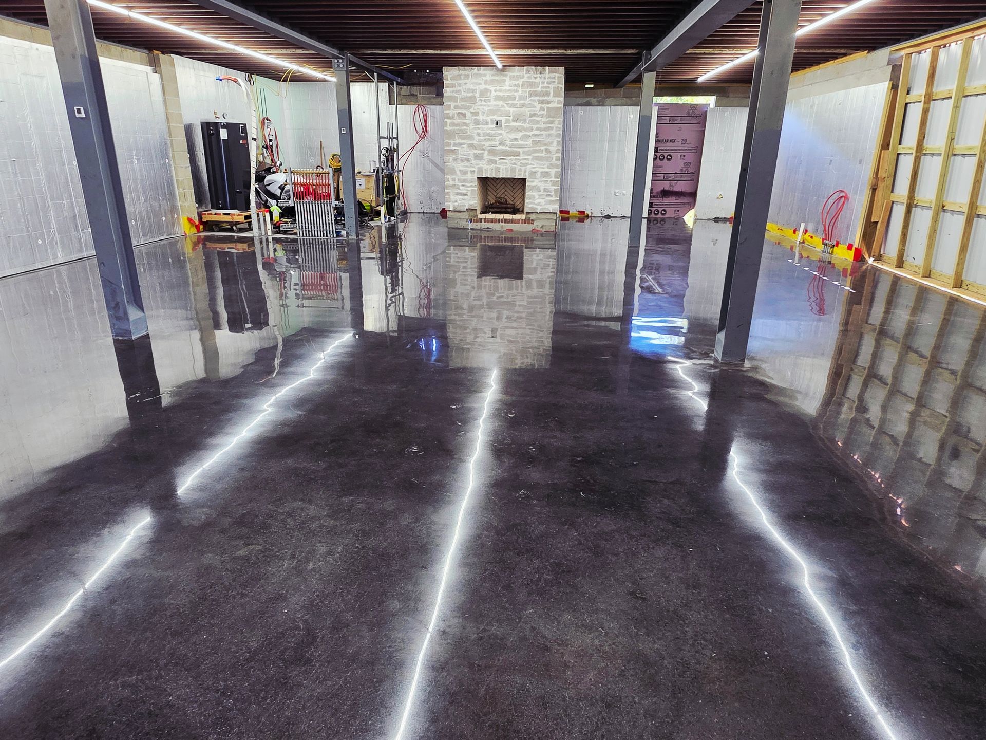 Empty polished warehouse interior with reflective black floor, exposed beams, and equipment along the walls