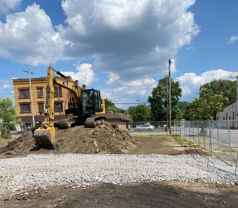 Construction equipment moving dirt beside a yellow building under a blue sky