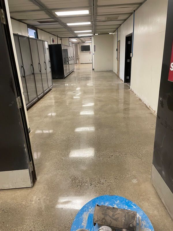 A polished concrete hallway with lockers on the left, doors on the right, and a floor-polishing machine in the foreground.
