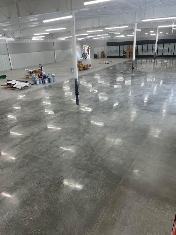 Large, empty commercial space with polished concrete floor, several support columns, and fluorescent lights.