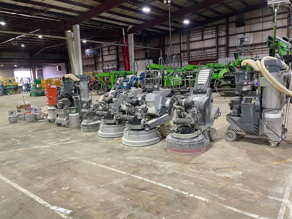 Grinding machines lined up on a concrete floor inside a warehouse. Various sizes and models are present.