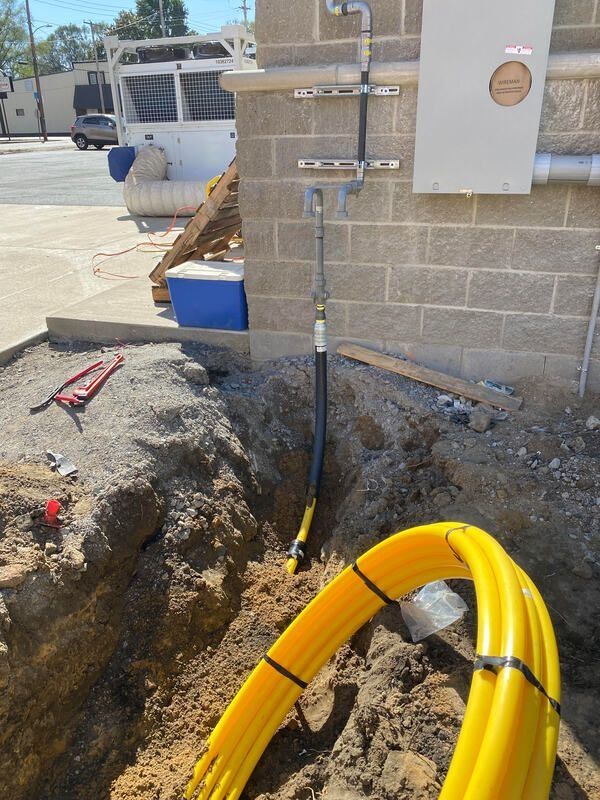 Construction site with yellow gas lines, piping on a brick wall, and a trench.