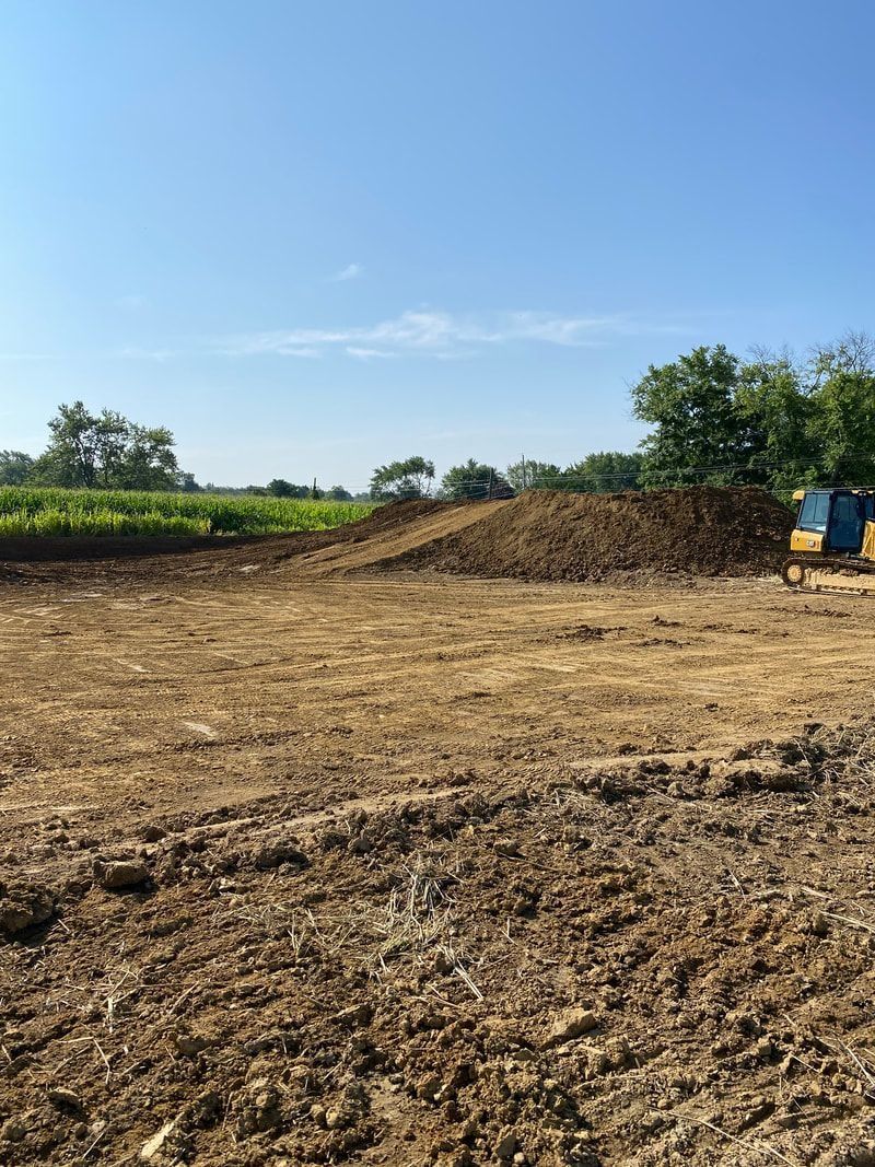 Dirt field with a large pile of dirt, blue sky, and trees in the background.
