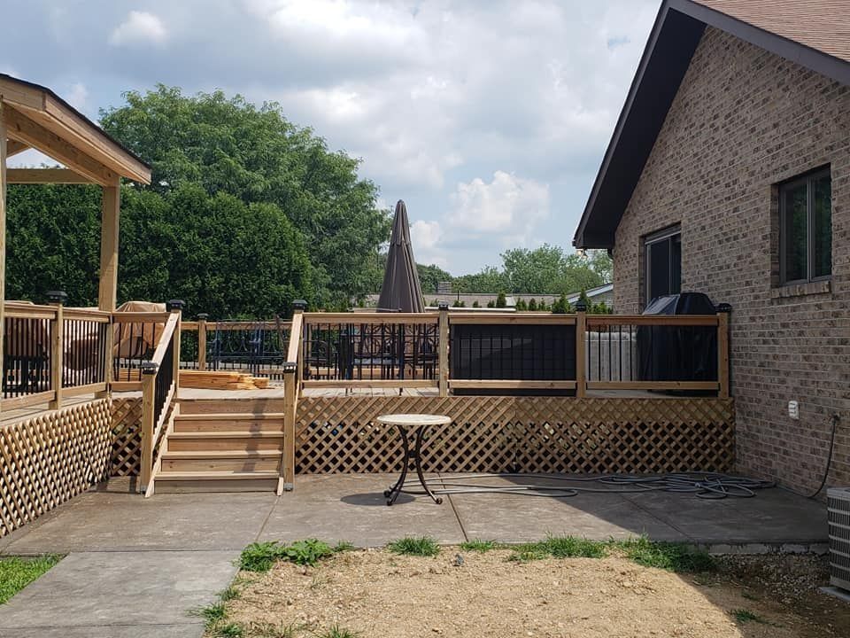 Backyard deck with wooden railing and lattice, leading to steps, and a table on a concrete patio.
