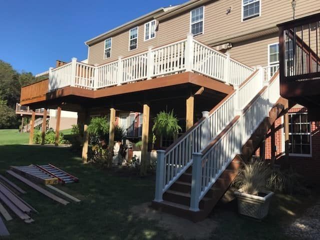 Two-level deck with white railings and brown steps, attached to a tan house on a lawn.