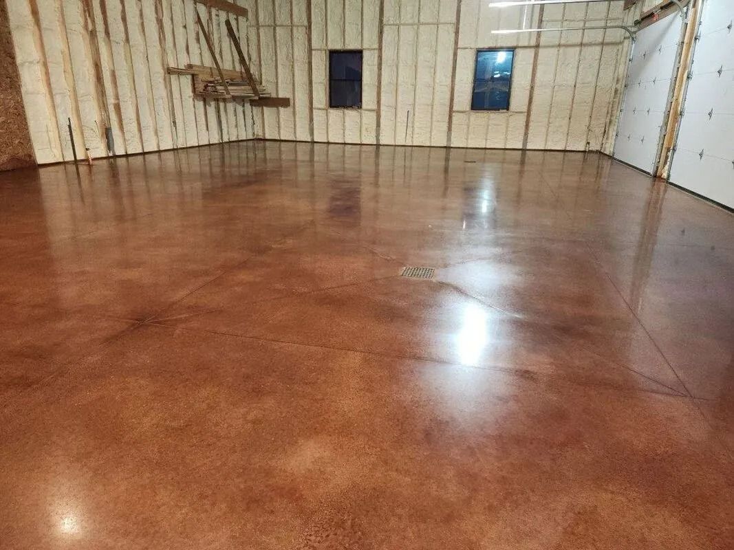 Brown stained concrete floor in an empty room, reflecting light. Wooden walls are visible.
