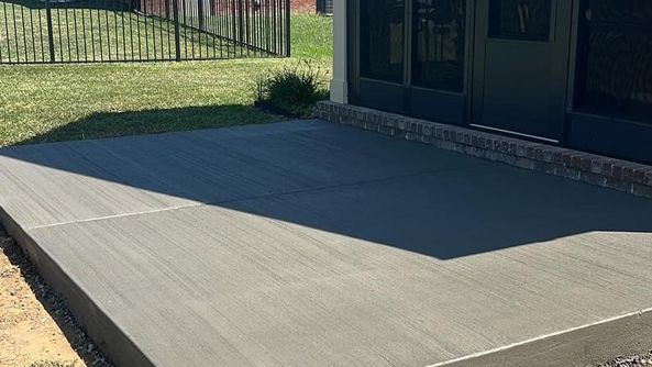 A concrete patio in front of a house with a fence in the background.