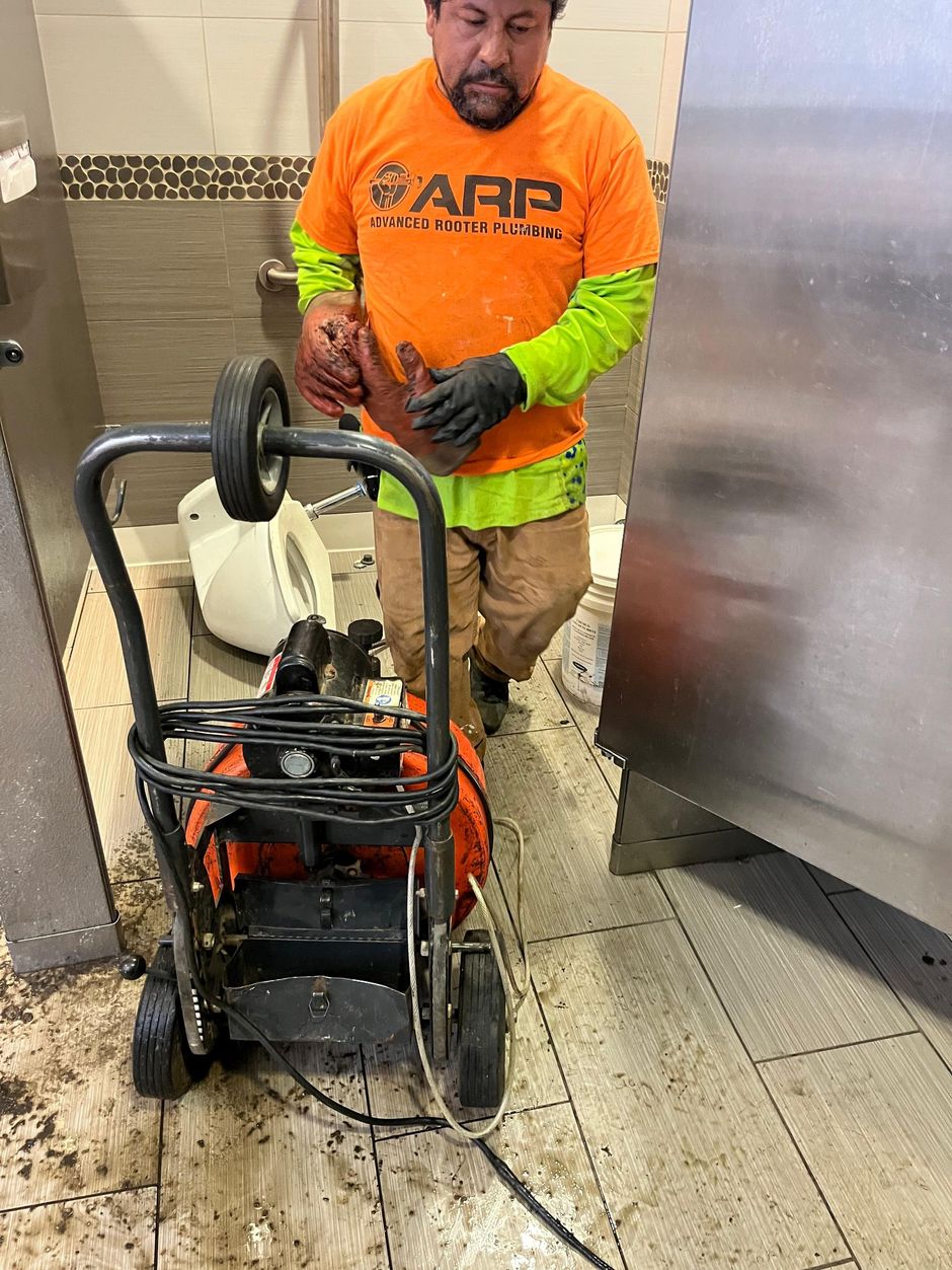 Worker in orange shirt adjusts a cart-mounted machine in a hallway.