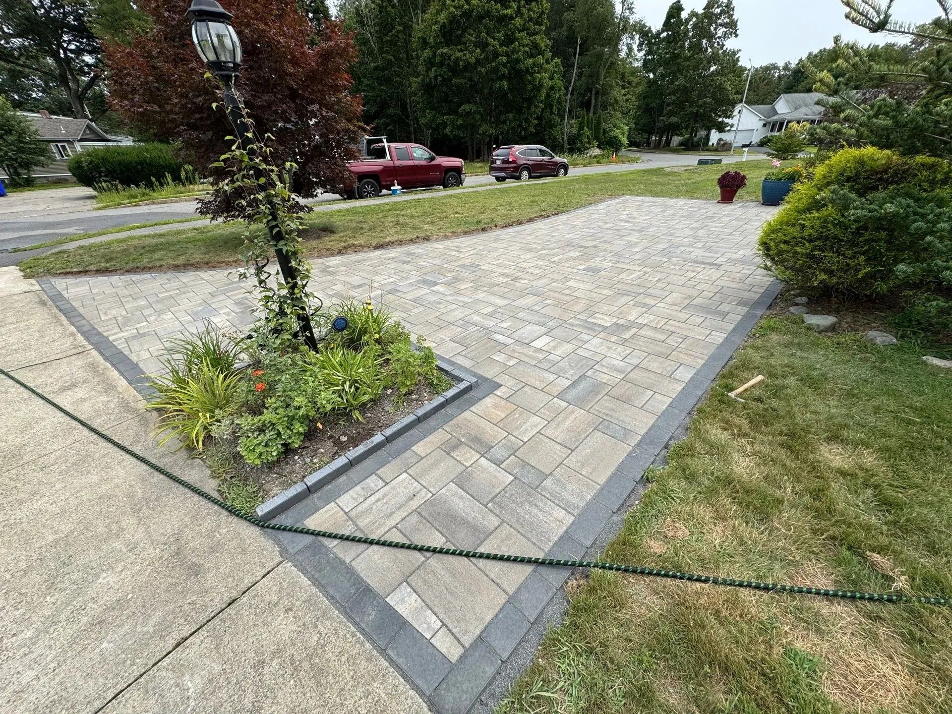 Stone walkway across a landscaped courtyard with trees, shrubs, and parked cars nearby.
