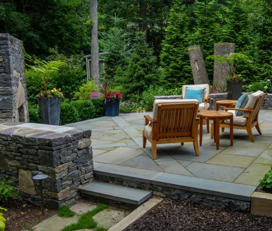 Stone patio with wooden chairs and table in a lush garden setting