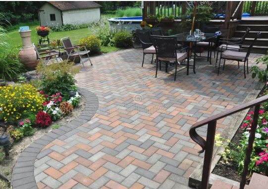 Patio with gray brick pavers, black outdoor table and chairs, and colorful flower beds by a house